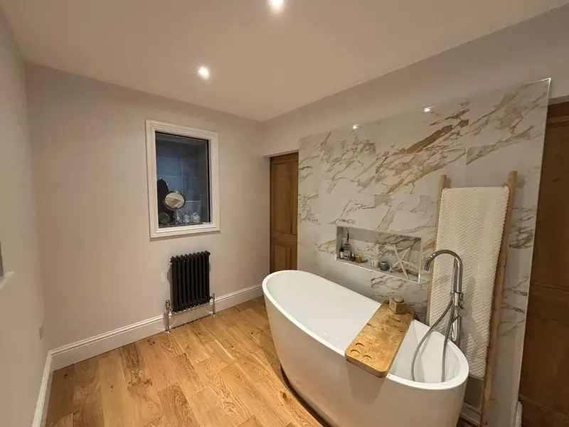 Bathroom with a white freestanding bath, a marble-effect wall panel with a niche, an oak floor and a column radiator