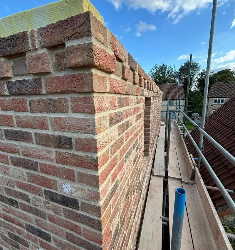 New red brick parapet with a stepped coping course, seen from the scaffold