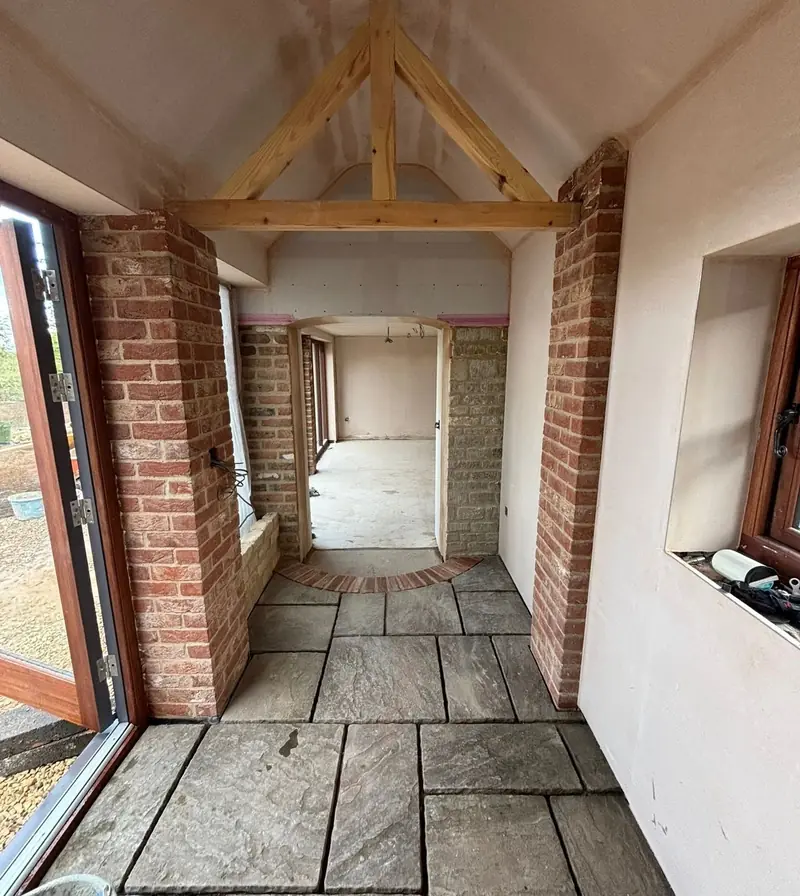 Conversion in progress: brick piers, an oak truss and a flagstone floor beside new glazed doors