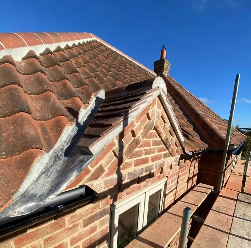 Clay pantile roof with a new brick dormer, lead flashing and scaffold, under a blue sky