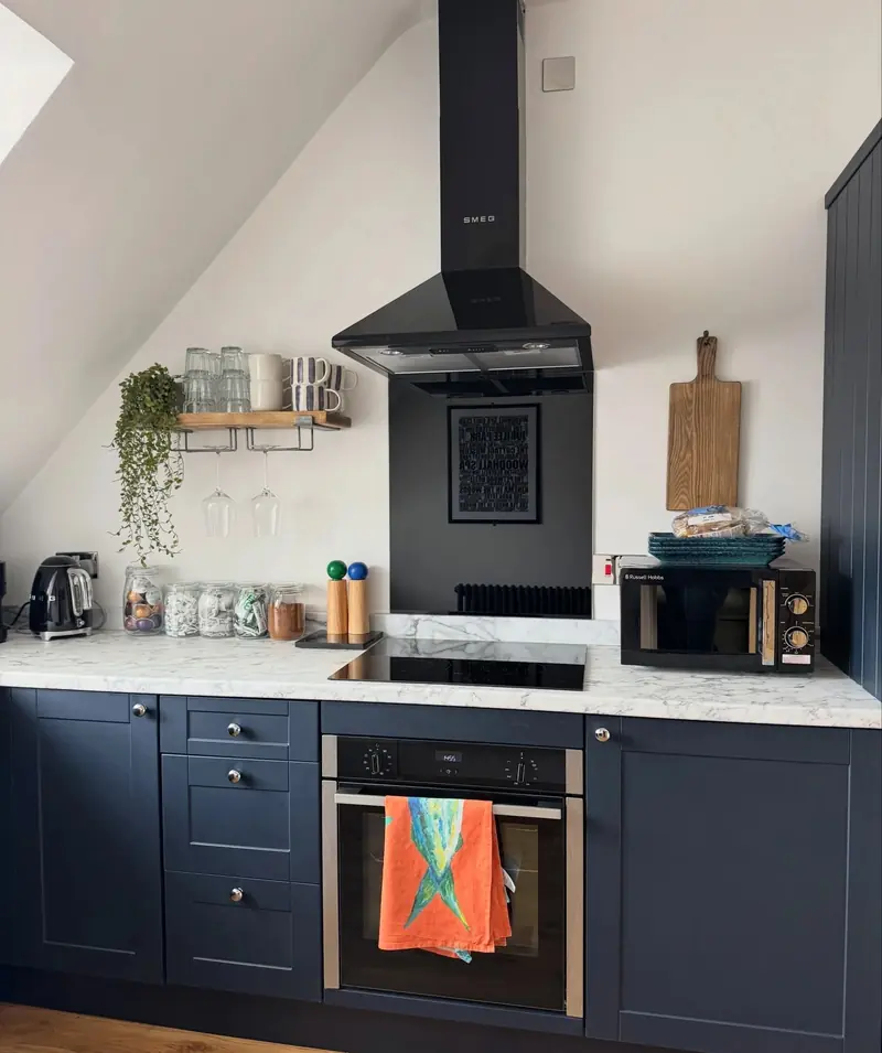 Navy shaker kitchen with a black chimney extractor, a built-in oven and a pale stone-effect worktop