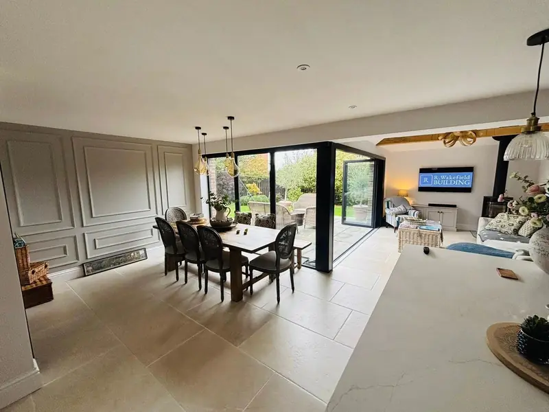 Dining area beside a panelled wall, opening into a living space with black-framed glazed doors to the garden