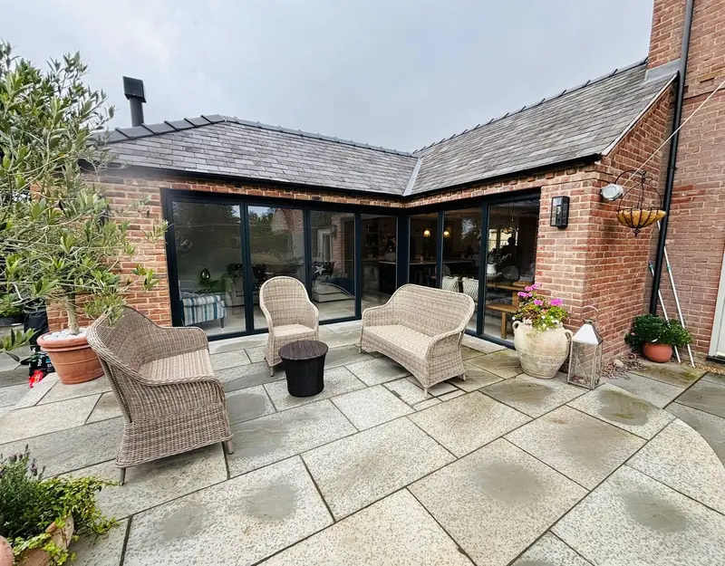 L-shaped single-storey brick extension with a slate roof and black-framed glazed doors around a stone patio
