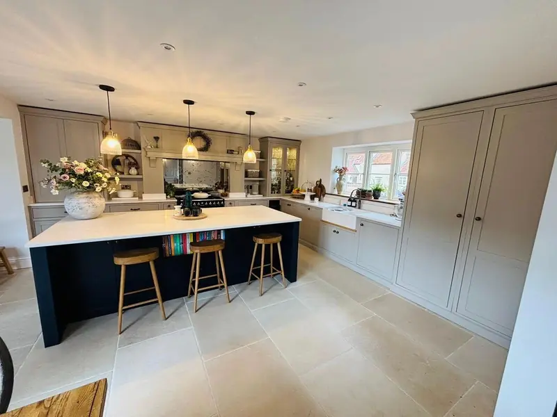 Kitchen with a dark island, bar stools, three pendant lights and pale shaker-style units