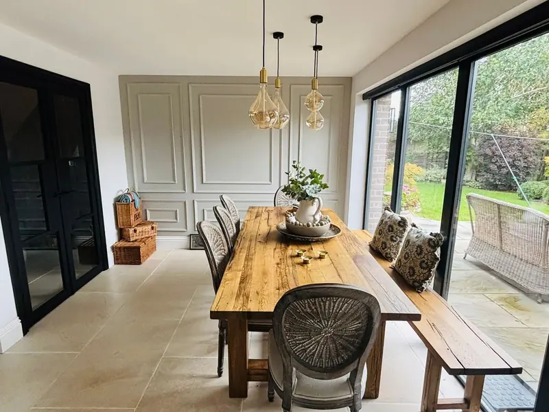 Oak dining table under pendant lights beside full-height black-framed glazing onto the garden