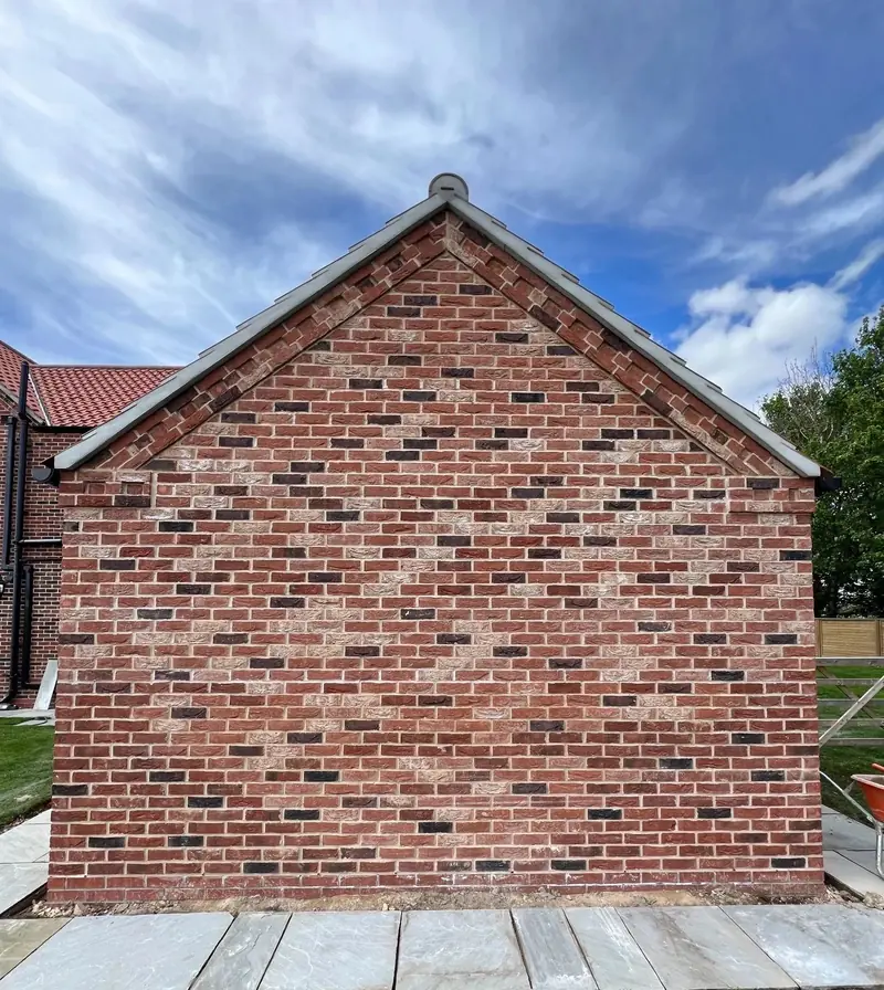 New red brick gable end with a stone coping and a paved path along its foot