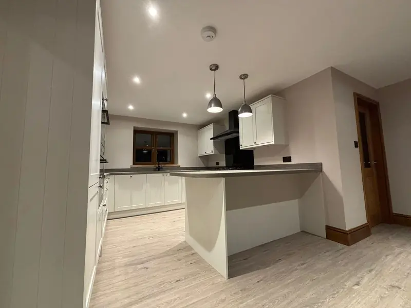 New kitchen with white shaker units, a peninsula with a grey worktop, two pendant lights and wood-effect flooring
