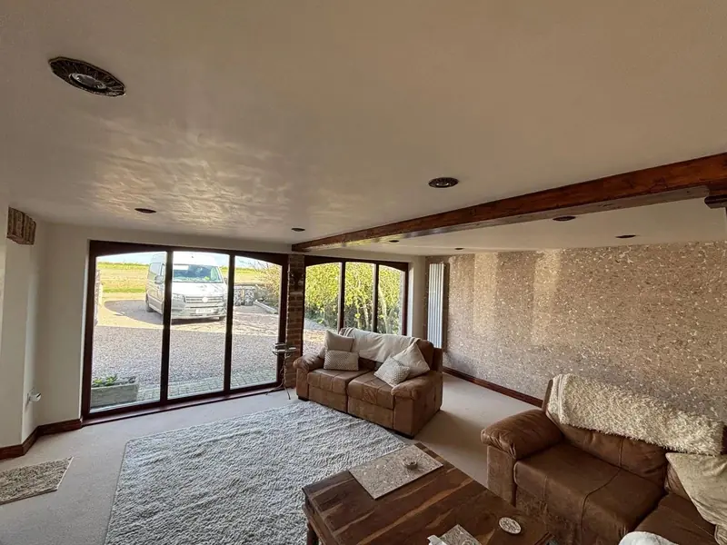 Living room with corner glazing, an exposed stone wall, a dark oak beam and leather sofas