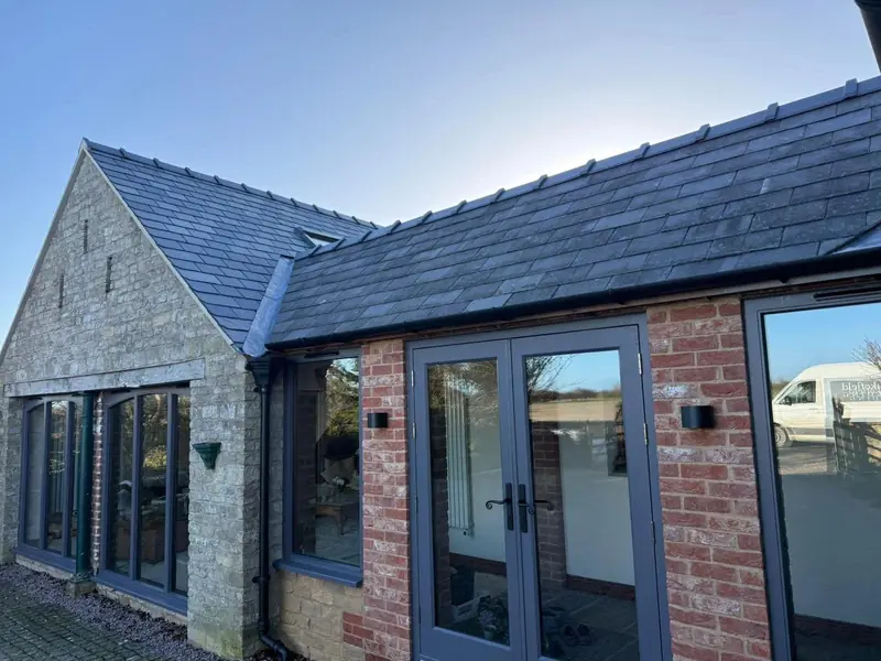 Stone and red brick single-storey extension with a slate roof and grey glazed doors