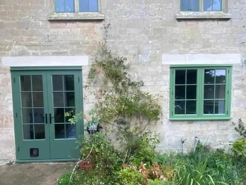 After: green painted timber French doors and a matching window under pale stone heads in the limestone wall