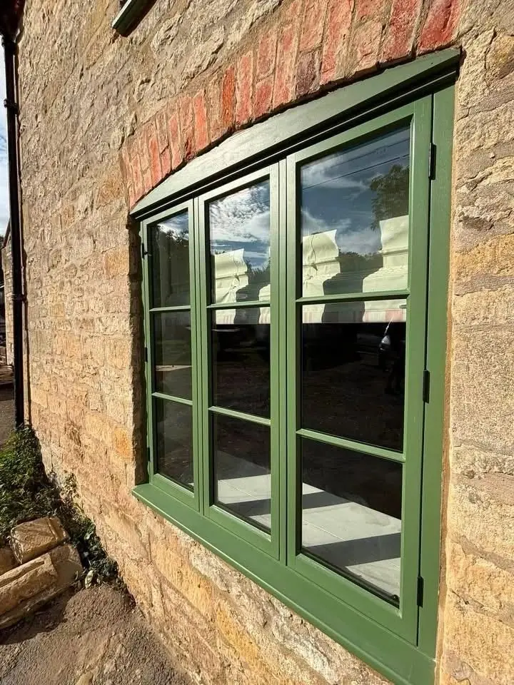 Green painted timber casement window set in a limestone wall with a red brick arch above